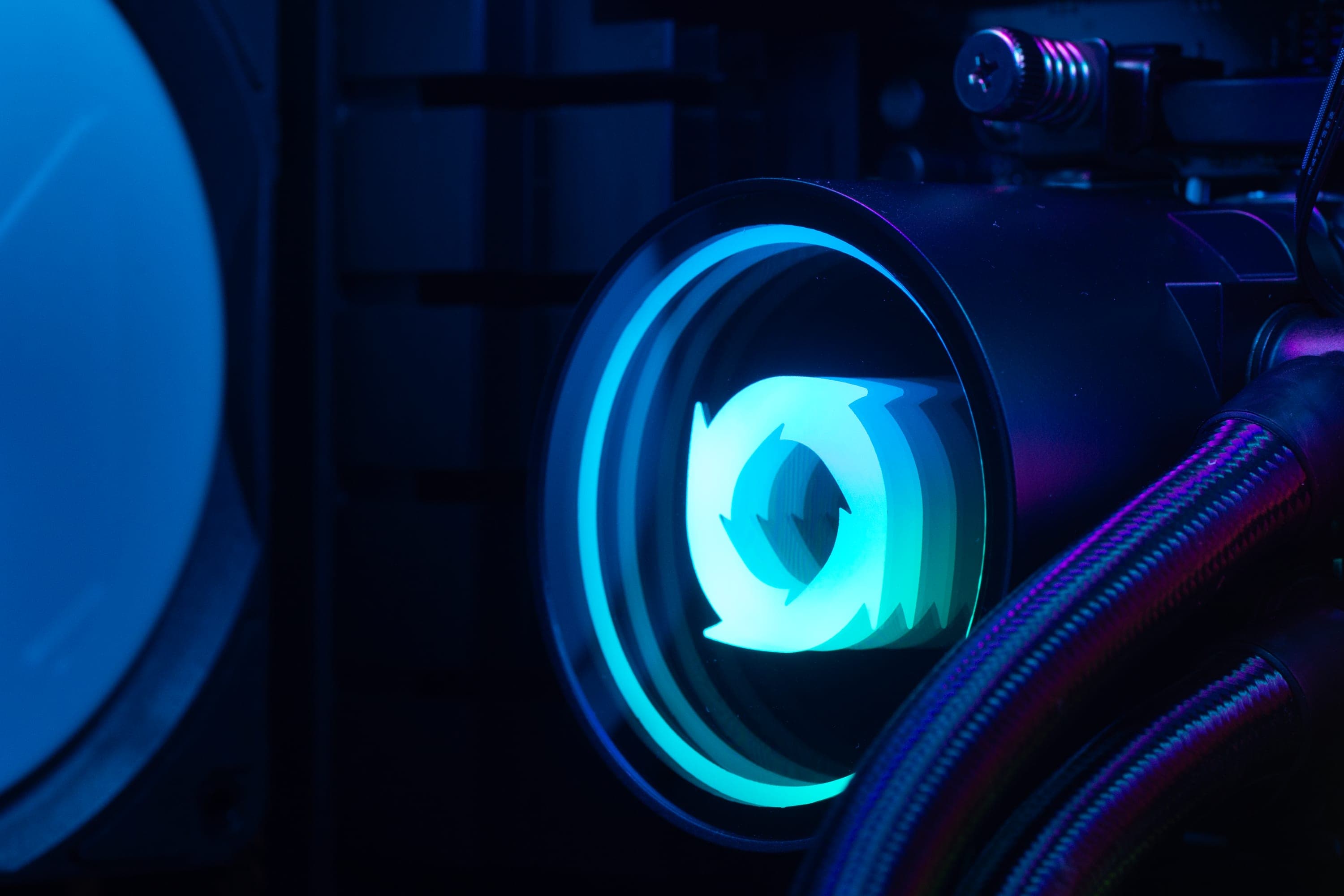 The pump block of a Typhoon 360 AIO cooler fitted in a build, the Typhoon mark lit in its cap, with braided coolant lines and a radiator fan behind.